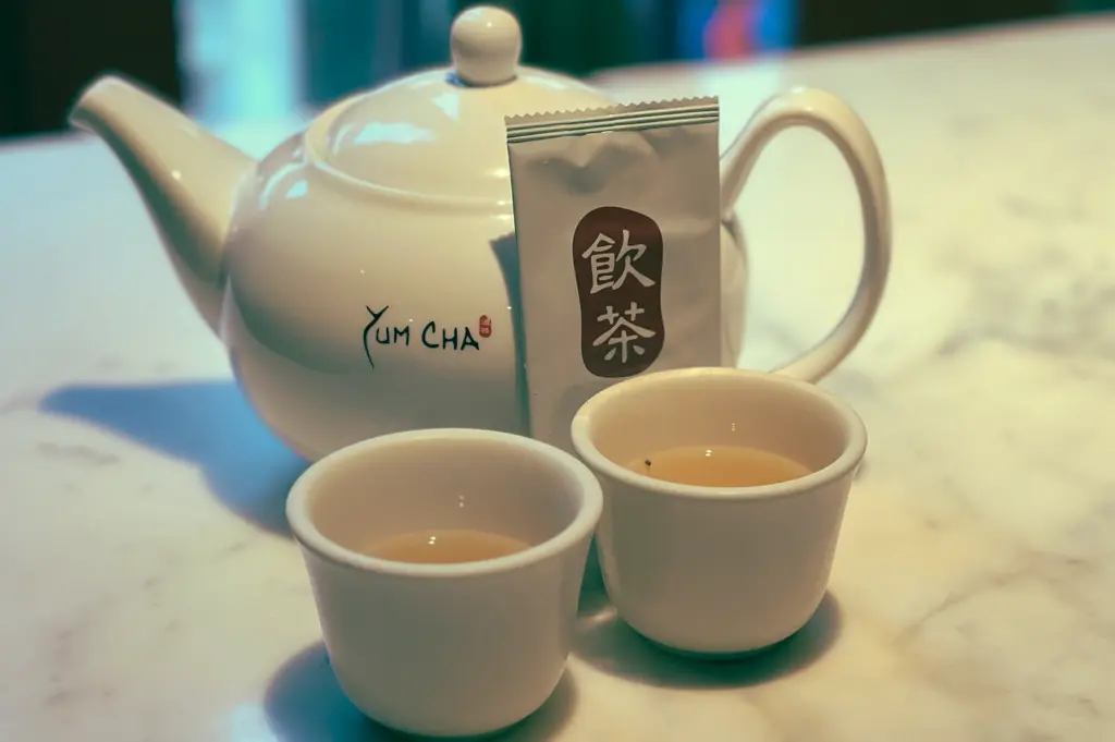 Close‑up, eye‑level view of a white porcelain Yum Cha teapot with two small tea cups on a marble table, representing the role of tea in a traditional Singapore yum cha dim sum meal.