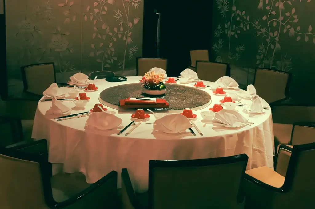 Eye-level wide shot of an elegant private Chinese dining room featuring a round banquet table set with white tablecloth, folded napkins, chopsticks, red sauce dishes, and a lazy Susan centerpiece, ideal for dim sum and fine dining in Singapore.