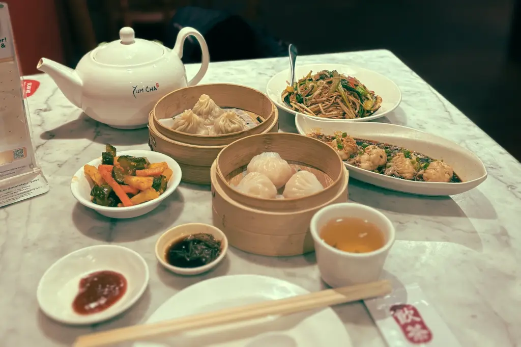 Slight overhead view of a Singapore yum cha table set with bamboo steamers of har gow and siew mai, plates of dim sum, and a white porcelain teapot, showing tea as the foundation of a traditional dim sum meal.