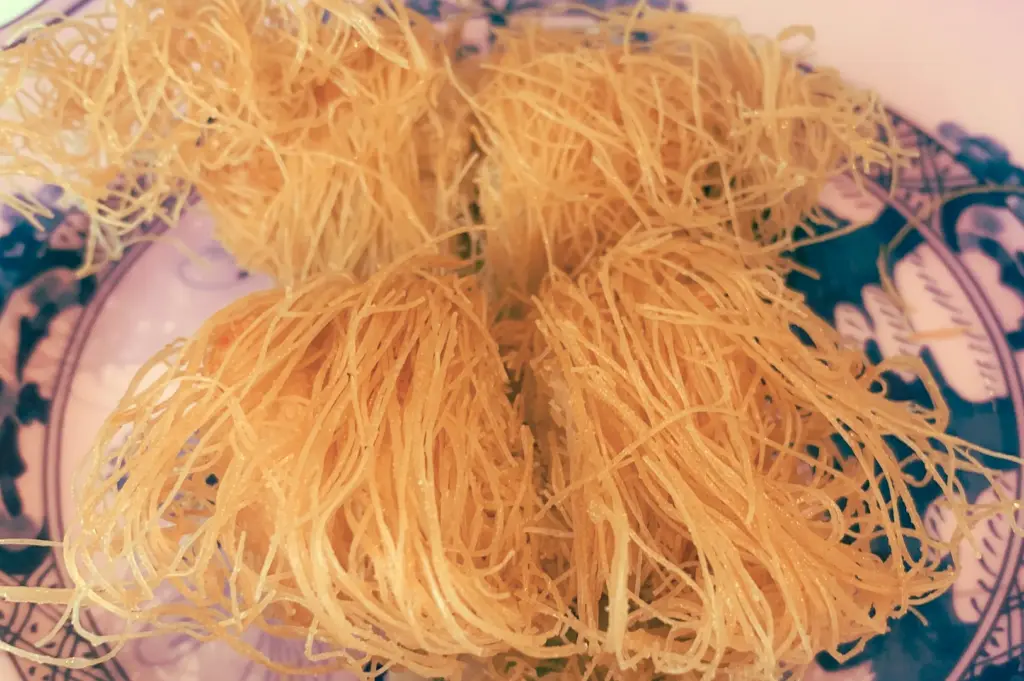 Overhead close-up shot of Pan‑fried Shredded Yam with Pumpkin, featuring golden, crispy yam strands arranged on a blue‑and‑white porcelain plate at Summer Pavilion, The Ritz‑Carlton, highlighting fine Chinese dessert craftsmanship and texture.