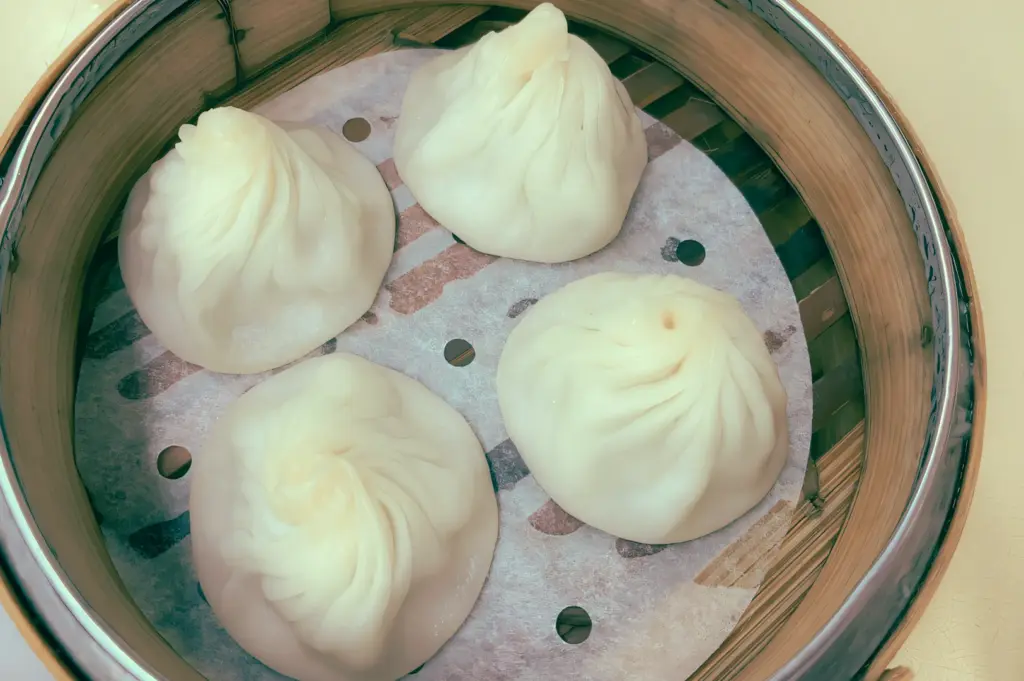 Top-down overhead shot of Shanghai xiao long bao soup dumplings in a bamboo steamer at Swee Choon Tim Sum Restaurant, Jalan Besar, showing pleated wrappers and classic steamed dim sum presentation in Singapore.