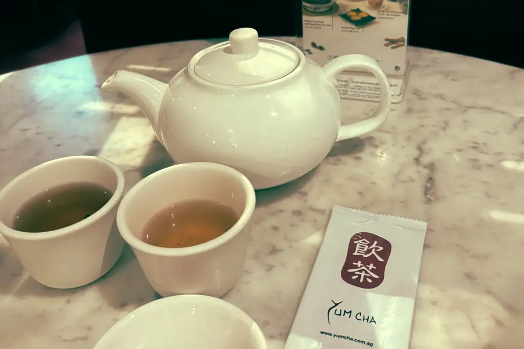 Eye‑level tabletop shot of a white porcelain teapot and two cups of Chinese tea at a Singapore yum cha restaurant, highlighting traditional tea service during a Cantonese dim sum meal.