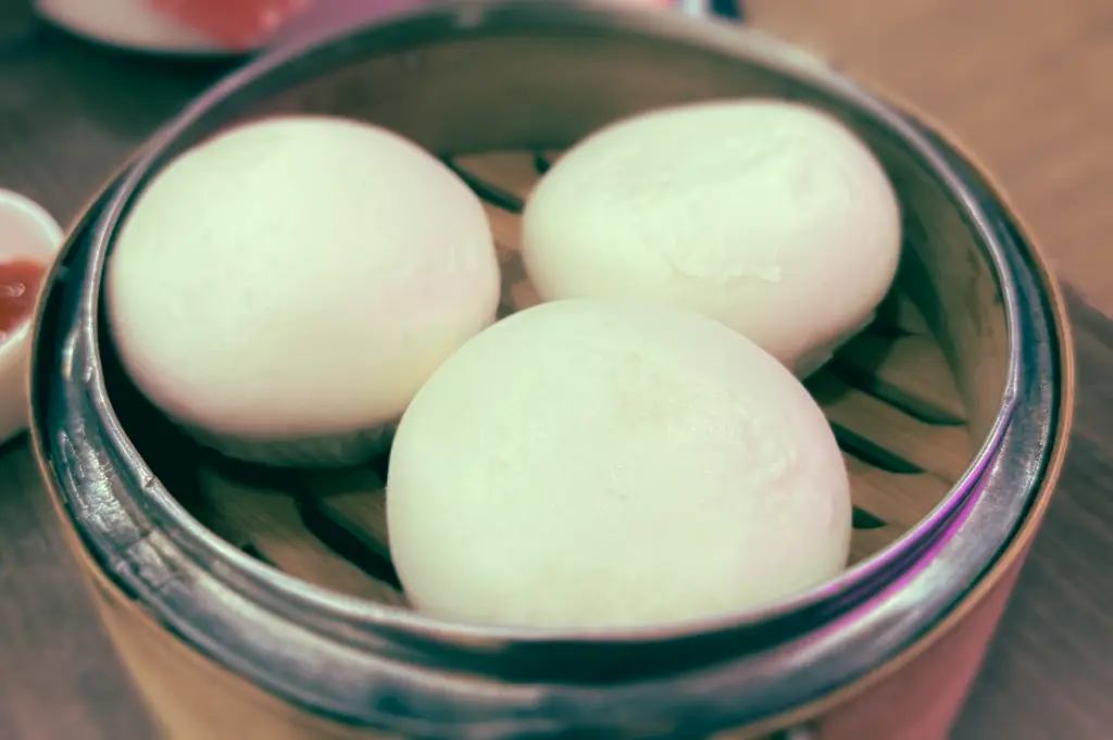 Eye-level close-up shot of steamed char siew bao in a metal steamer at Swee Choon Tim Sum Restaurant, featuring soft white buns served as classic Hong Kong-style dim sum in Singapore.