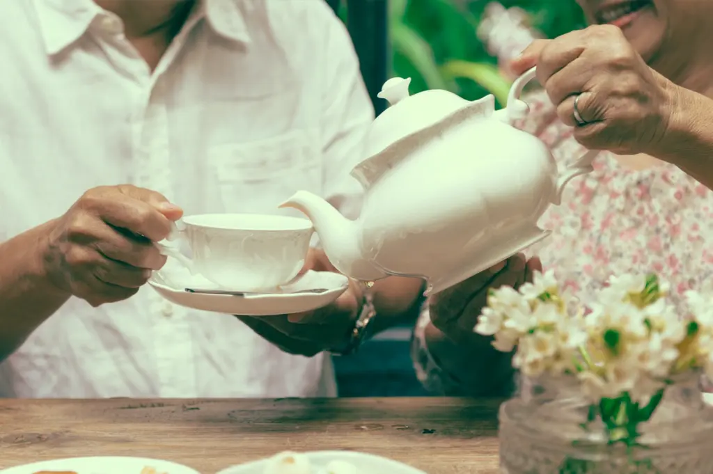 Medium close-up shot of one diner pouring tea for another at a shared table, illustrating the yum cha tradition of serving others before oneself as a gesture of respect and care.