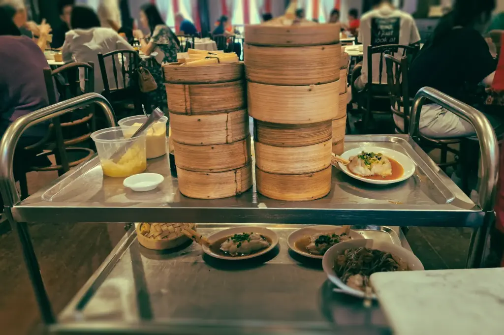 Eye‑level view of stacked bamboo steamers on a traditional dim sum cart in a busy Singapore yum cha restaurant, reflecting the communal and interactive nature of Cantonese dining.