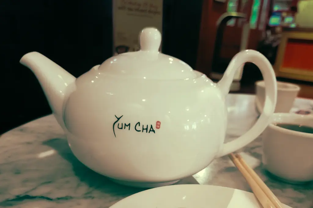 Front‑facing close‑up of a white porcelain Yum Cha teapot on a marble table, symbolizing the central role of tea in a traditional Singapore yum cha dim sum experience.