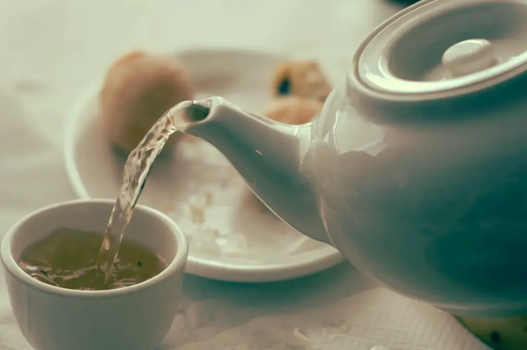 Close‑up action shot of hot Chinese tea being poured from a porcelain teapot into a small cup, capturing the tea‑pouring ritual that paces a traditional yum cha dim sum meal in Singapore.