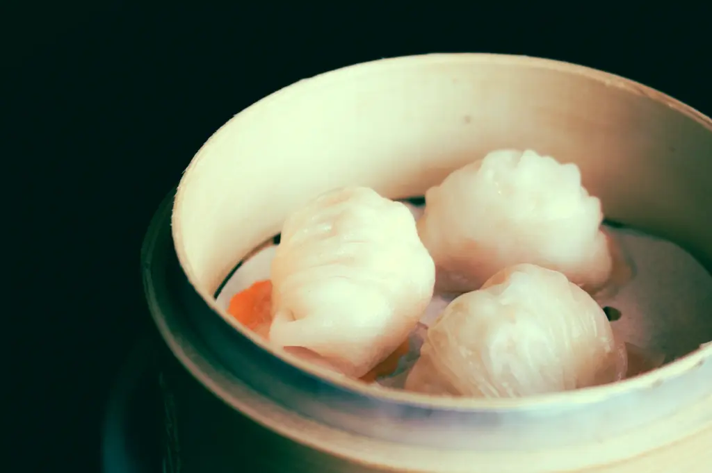 Close-up angled view of steamed har gow shrimp dumplings inside a bamboo basket, highlighting glossy translucent wrappers, pleated edges, and classic dim sum presentation in Cantonese cuisine