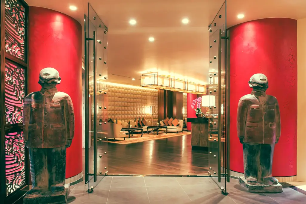 Luxury Chinese restaurant entrance lobby with red accent walls, modern Asian statues, glass doors and warm ambient lighting – wide-angle front shot