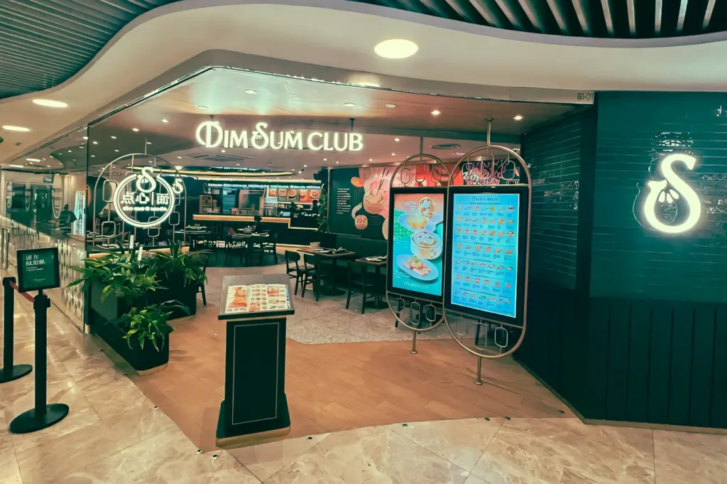 Wide-angle front-facing shot of Dim Sum Club at Wheelock Place, Orchard Road Singapore, showing illuminated signage, digital menu boards, and casual mall dining entrance