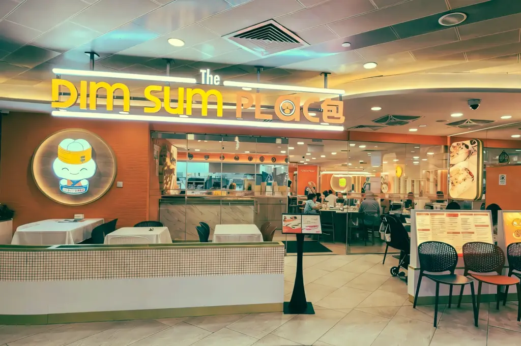 Eye-level wide angle shot of The Dim Sum Place Centrepoint storefront in Orchard Road Singapore, casual halal dim sum restaurant with bright signage and dining area