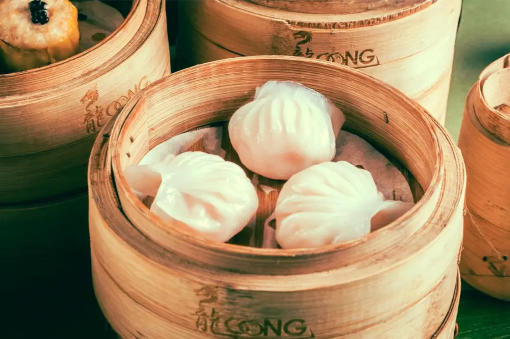 Steamed shrimp dumplings (har gow) in traditional bamboo baskets alongside assorted dim sum, captured in a warm-toned close-up overhead angle for an authentic Cantonese dining and halal dim sum experience.