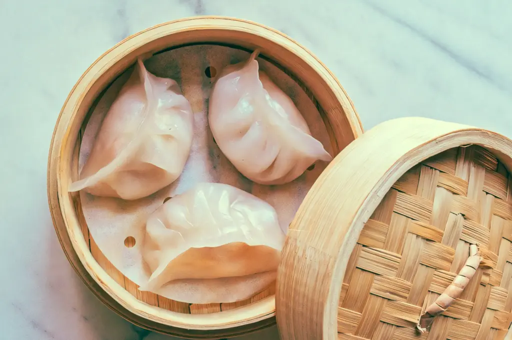 Top-down view of traditional Cantonese har gow in a bamboo steamer, featuring three translucent shrimp dumplings with delicate pleats, showcasing authentic dim sum craftsmanship and fresh seafood texture