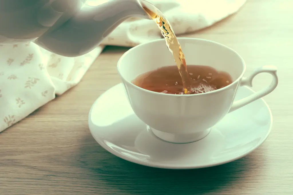 Close-up side angle of hot tea being poured from ceramic teapot into white cup, highlighting central role of tea in traditional yum cha culture