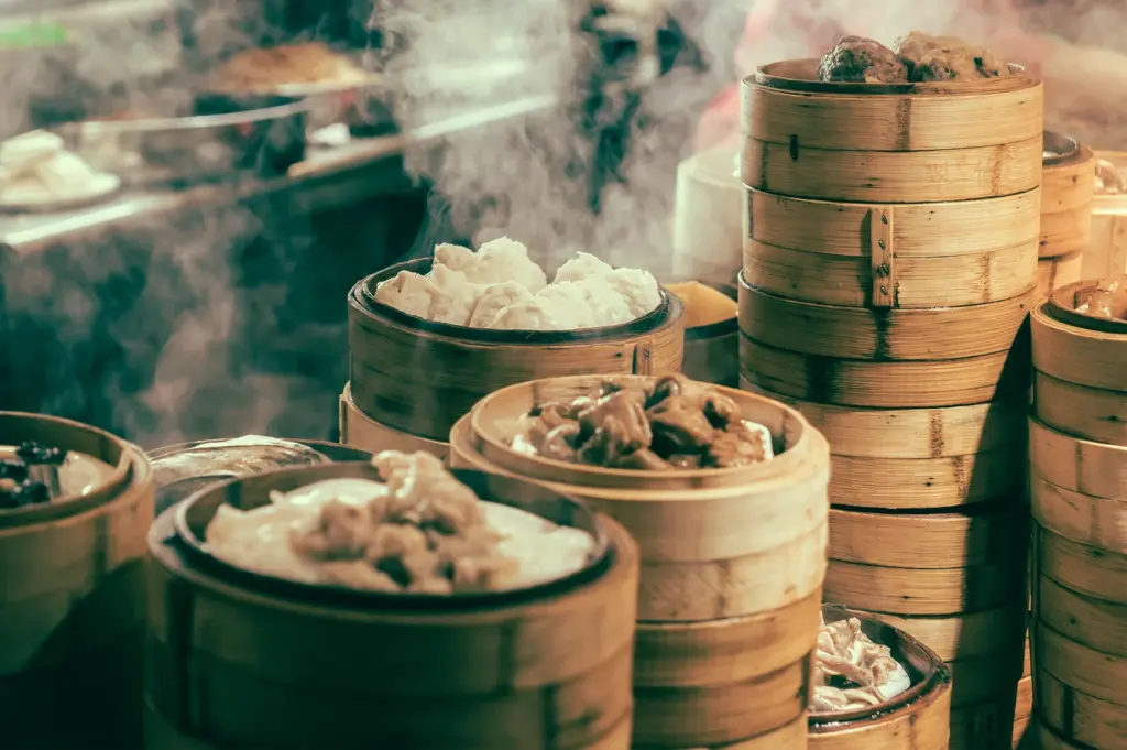Three-quarter angle medium shot of stacked bamboo steamers releasing steam over different dim sum items, illustrating high-volume preparation and temperature control in dim sum kitchen operations