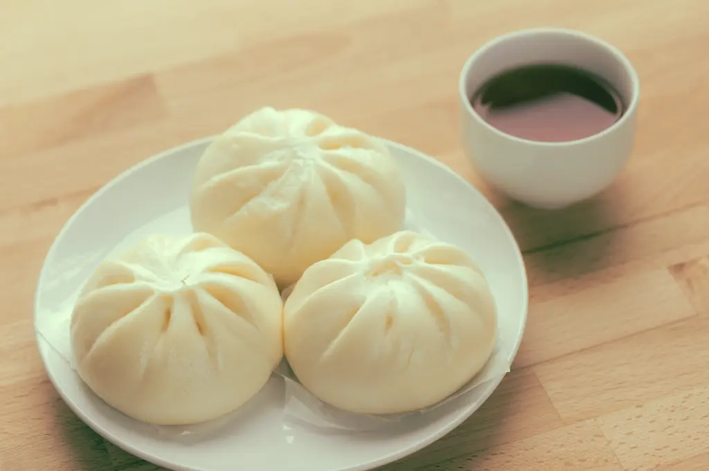 Top-down overhead shot of steamed bao buns on white plate with tea cup, representing simple dim sum as light accompaniment to tea