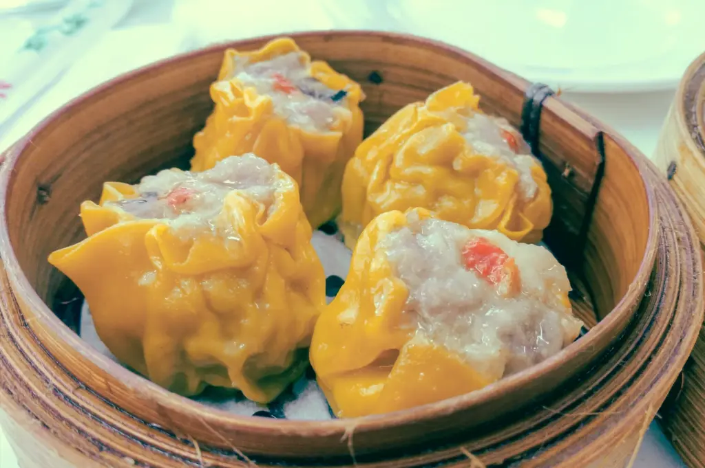 Slight high-angle close-up shot of steamed siew mai pork dumplings in a bamboo basket, showing glossy wrappers and balanced fat-to-meat texture for authentic Cantonese dim sum