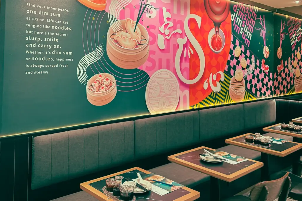 Eye-level interior shot of Dim Sum Club seating with colorful dim sum mural wall, cushioned bench tables, and casual cafe-style dining setup in Orchard Road