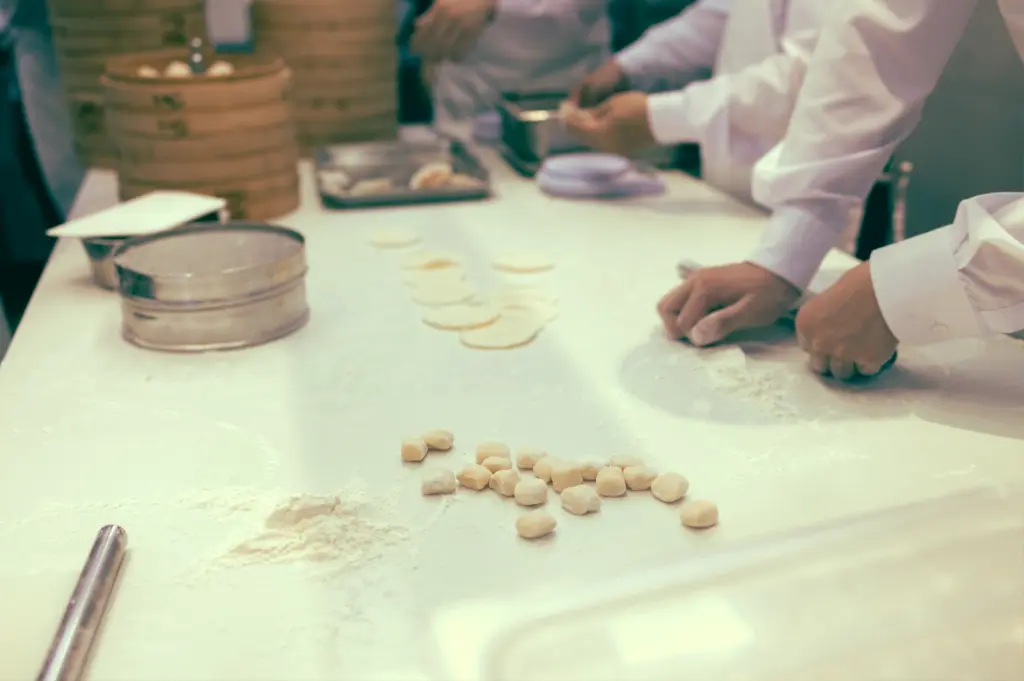Over-the-shoulder close-up shot of chefs preparing dim sum dough portions on a floured workstation, emphasizing labour-intensive preparation and skilled dim sum craftsmanship
