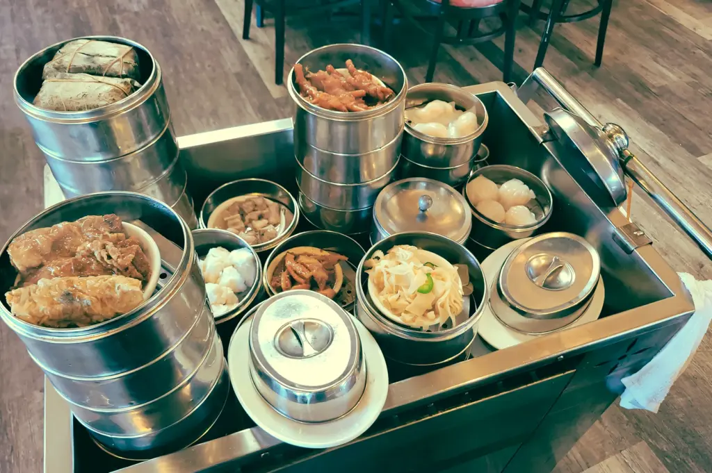 Slight high-angle shot of a dim sum service cart filled with metal steamers and assorted dishes, representing traditional pushcart service model and restaurant operations.